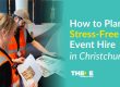 Two event professionals wearing orange safety vests review event layout plans inside a modern venue. Text overlay reads “How to Plan Stress-Free Event Hire in Christchurch” with the Theme Productions logo.